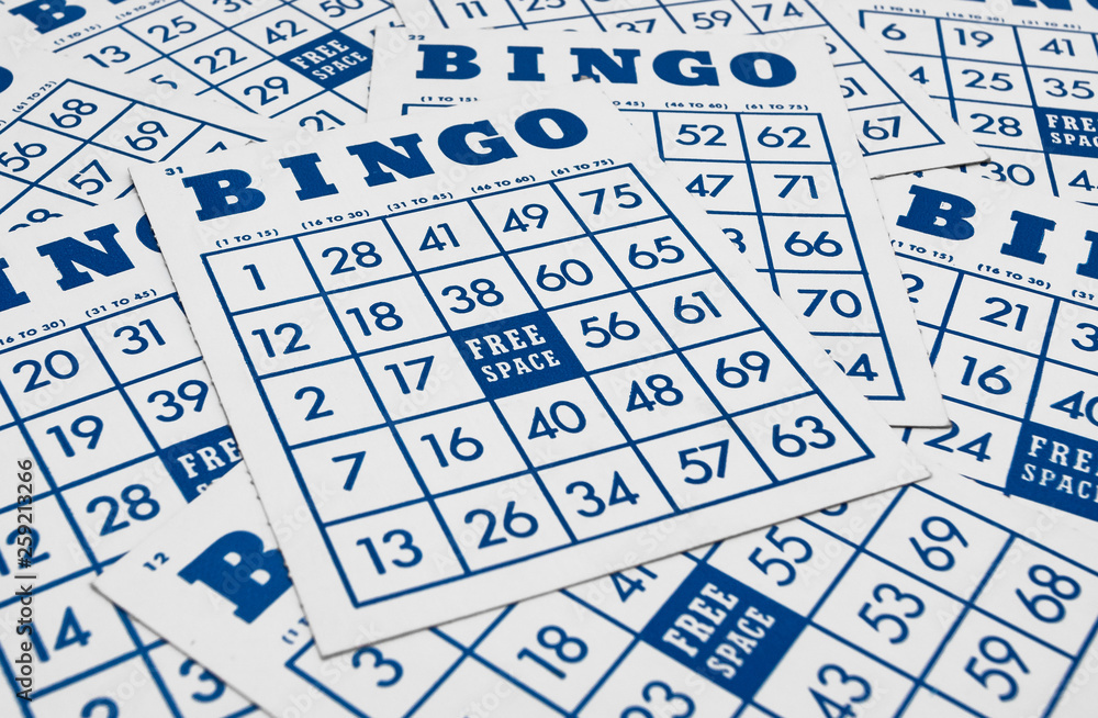 A close-up photo of multiple Bingo cards scattered on a surface. Each card features a grid of numbers with the word "BINGO" at the top and a "FREE SPACE" in the center. The numbers and letters are printed in blue ink on white cards.