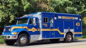 A blue and yellow Broughton rescue truck marked with "Rescue 270" and the number "43" is parked on the side of a road. The truck is surrounded by lush green trees.