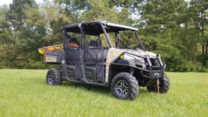 An all-terrain utility vehicle with emergency rescue equipment mounted on the rear is parked on a grassy field. The vehicle has four seats, a winch on the front bumper, and is marked with "Station 2-81" on the side. Trees are visible in the background.